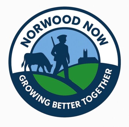 A blue and white circle with a graphic of a minuteman and an oxen. The words Norwood Now and Growing better together encircle the graphic.